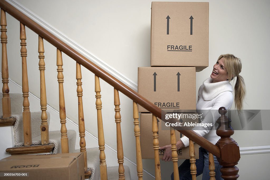 Woman carrying stack of boxes up stairs, smiling, side view