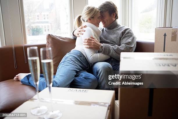 couple embracing on sofa surrounded by boxes and two champagne flutes - bay window interior stock pictures, royalty-free photos & images