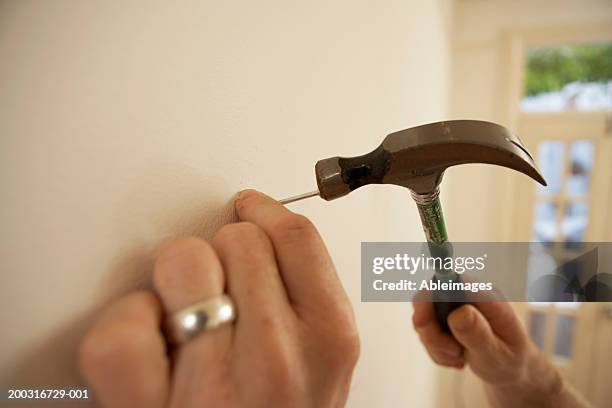 man hammering nail into wall, close-up - hammer and nail fotografías e imágenes de stock