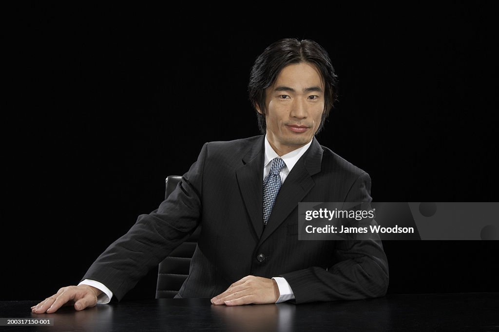 Businessman sitting at desk, leaning to one side, smiling, portrait