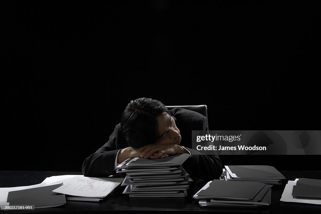 Businessman asleep at desk resting head on stack of files