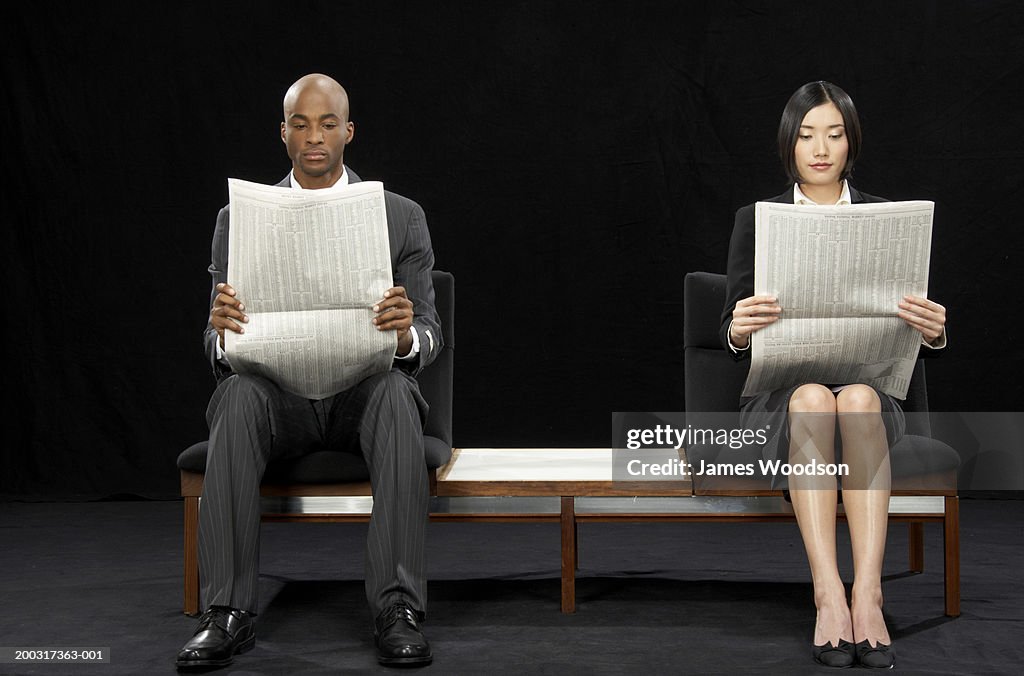 Businessman and businesswoman sitting on bench, reading newspapers