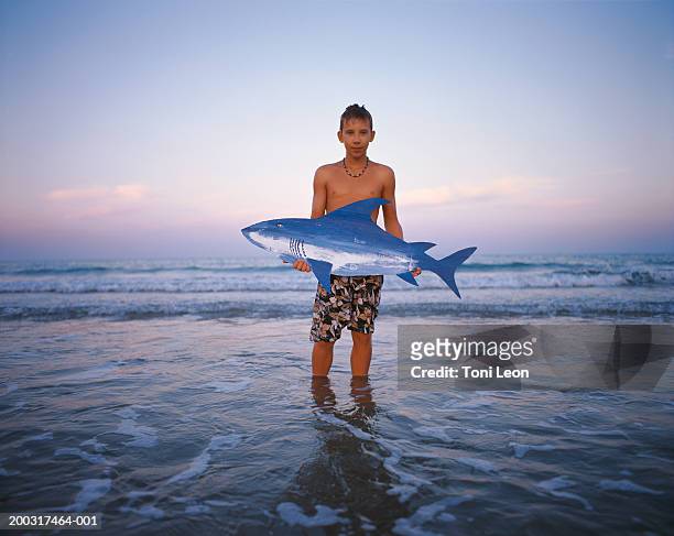 boy (10-12) standing in sea, holding cardboard shark, portrait - plastikhai stock-fotos und bilder