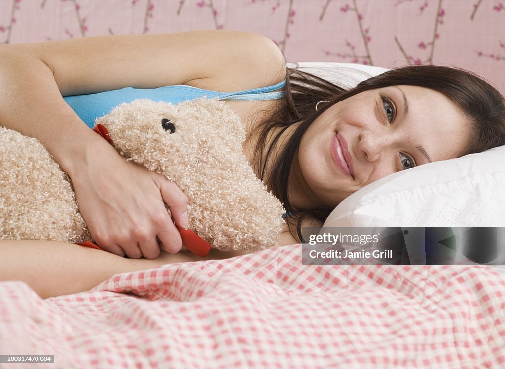 Young woman lying in bed with teddy bear