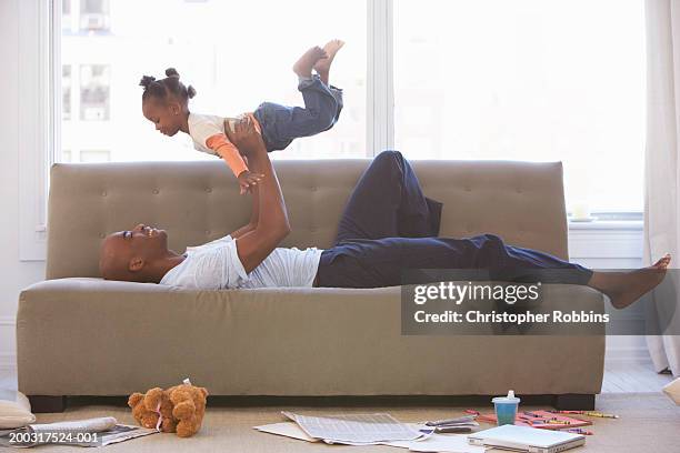 father lying on sofa, holding daughter (2-4) up - lying on back girl on the sofa stock pictures, royalty-free photos & images