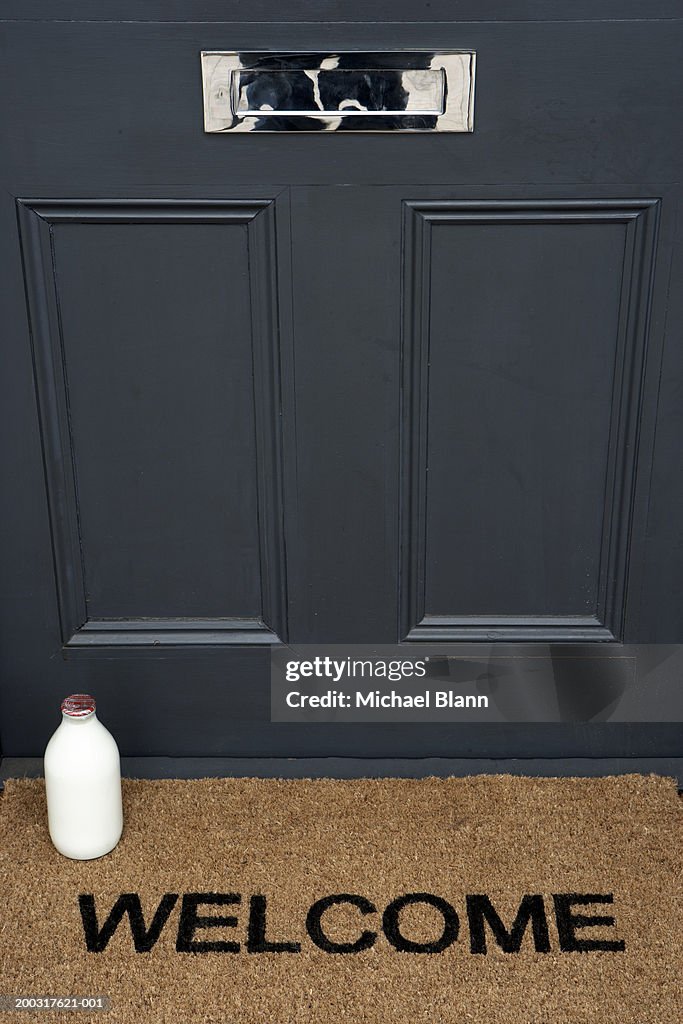 Milk bottle on welcome mat by front door, close-up