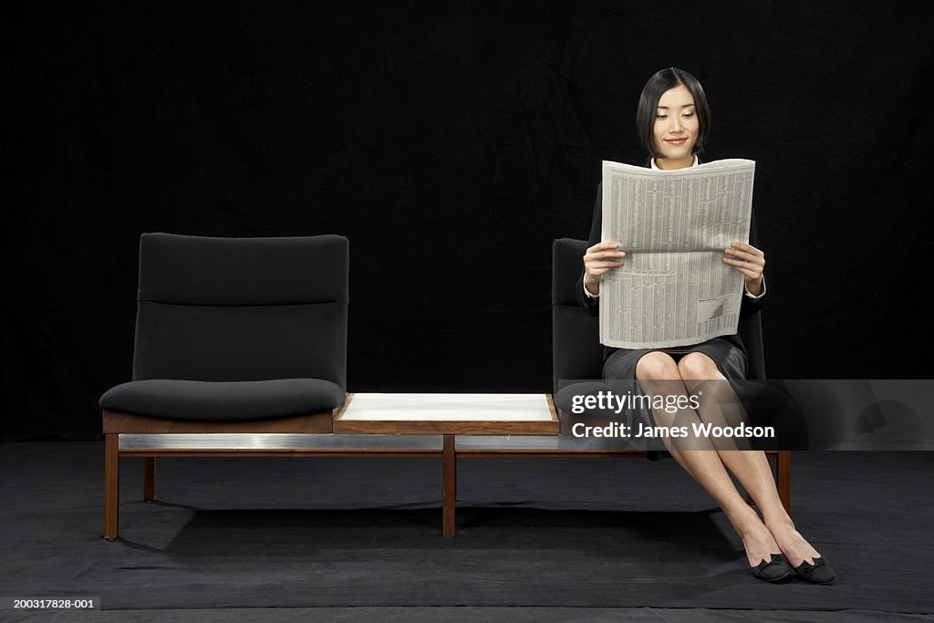 Businesswoman sitting on bench reading newspaper, smiling