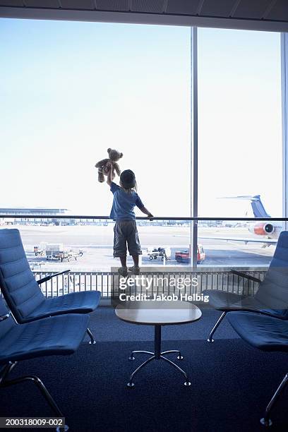 boy (3-5) standing at window in airport lounge holding teddy bear - holding above head stock pictures, royalty-free photos & images