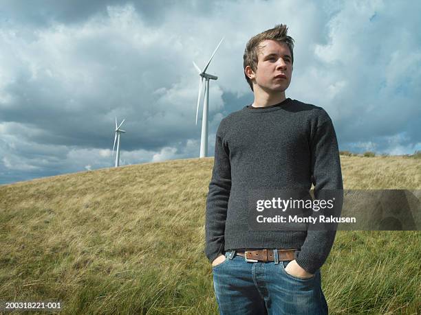 young man standing in field, wind turbines in background - green pants stock-fotos und bilder