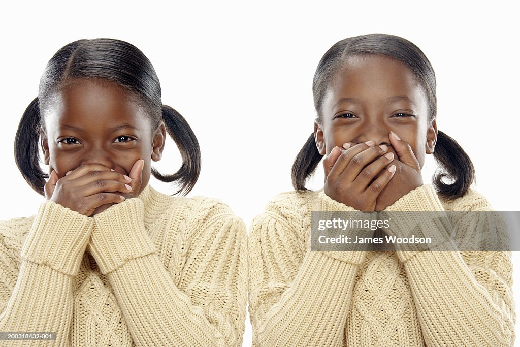 Twin girls (7-9) covering mouths with hands, portrait, close-up