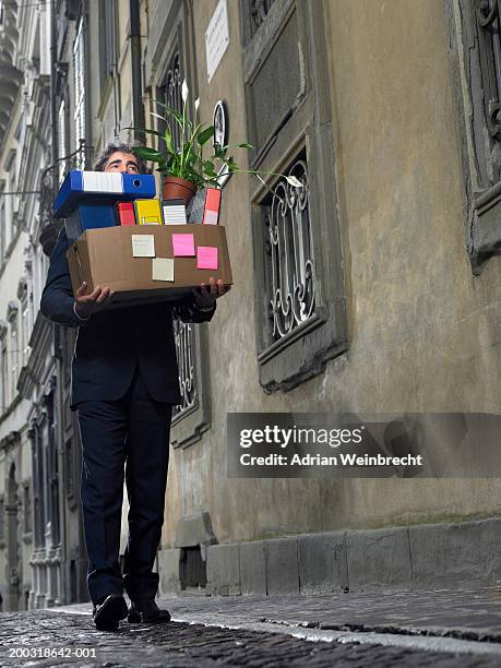 mature businessman carrying box of office files in street - map street stockfoto's en -beelden