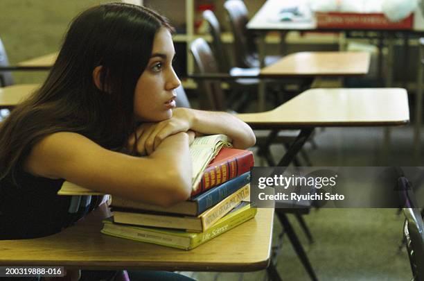 young woman sitting in library desk, leaning on books, side away - edificio de escuela secundaria fotografías e imágenes de stock