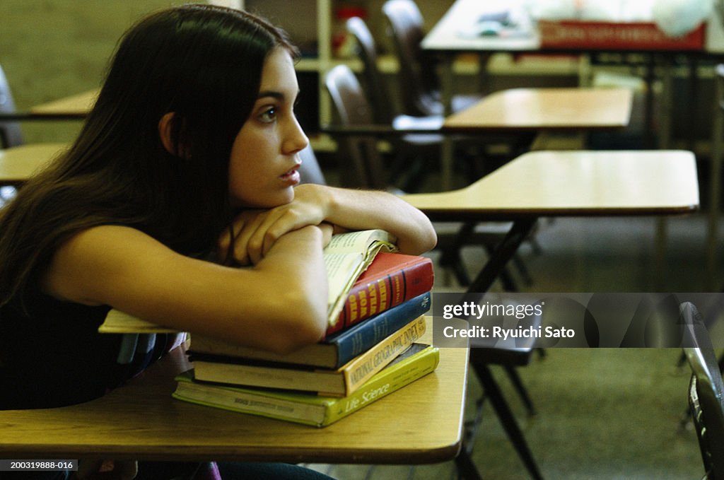 Young woman sitting in library desk, leaning on books, side away