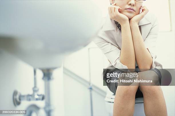 woman sitting on toilet bowl with hand on chin, mid section - restroom sign 個照片及圖片檔