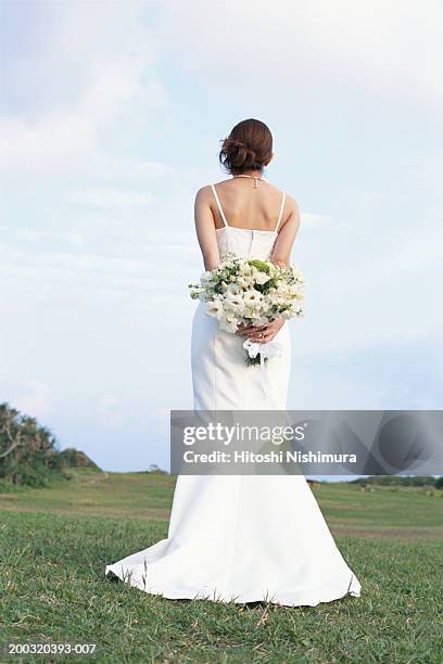 bride holding bouquet in field, rear view - bruid stockfoto's en -beelden