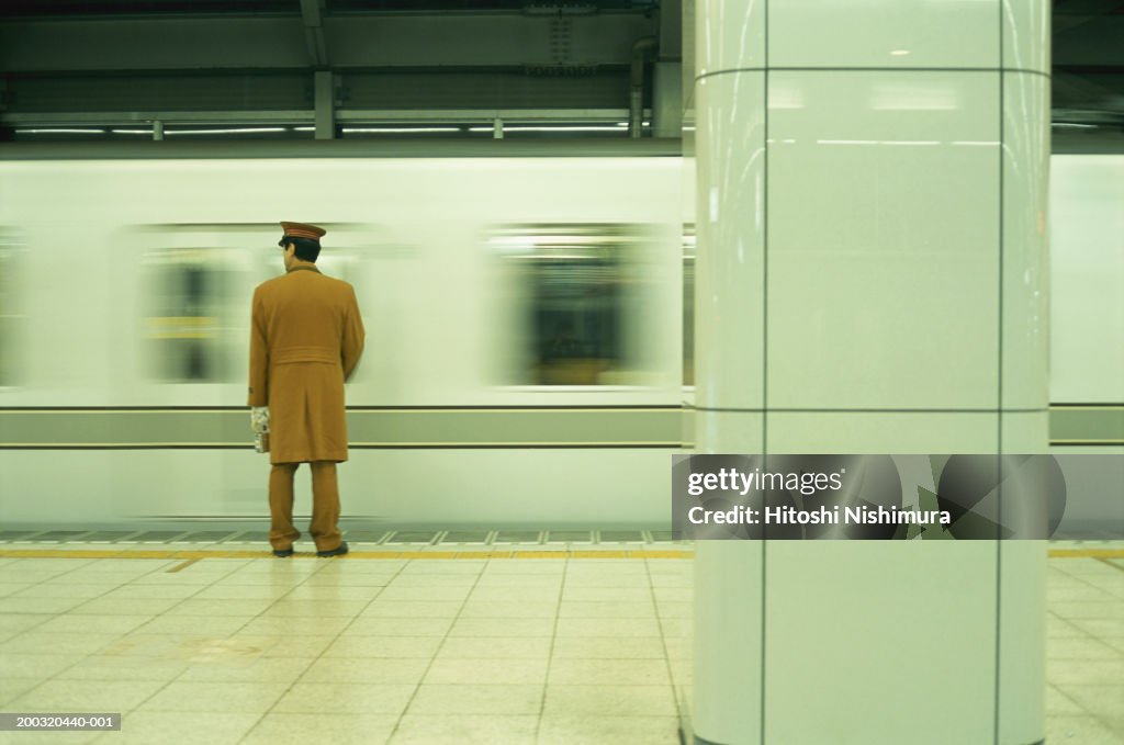 Police officer standing on railway platform, rear view