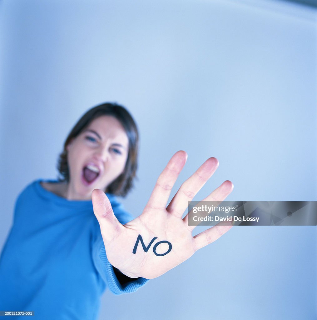 Young woman showing 'NO' written on hand, focus on hand