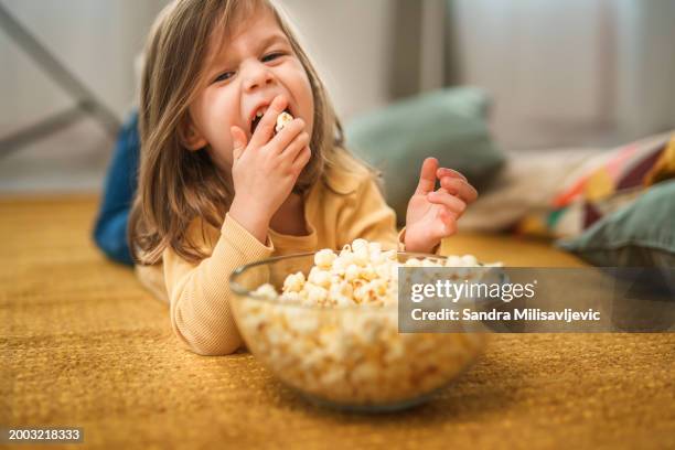 one toddler girl lying on the floor at home and eating popcorns - popcorn floor stock pictures, royalty-free photos & images