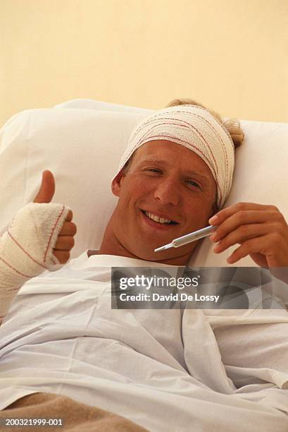 male patient in hospital bed, holding thermometer, smiling - injured man in hospital bed stockfoto's en -beelden