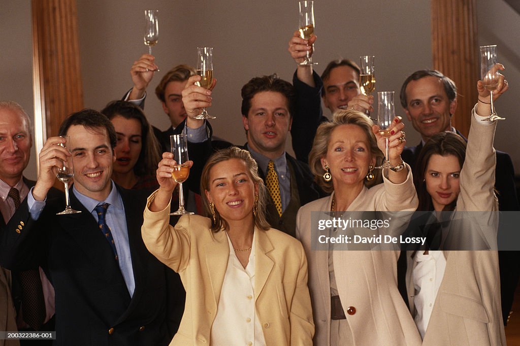 Business people raising glasses in office, smiling