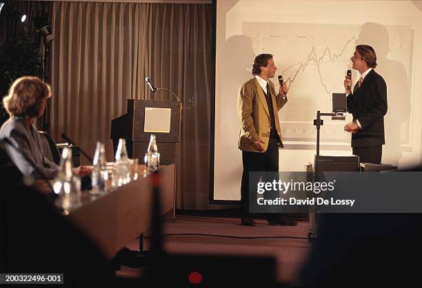 two businessmen holding microphone in conference room, face to face - overheadprojektor stock-fotos und bilder