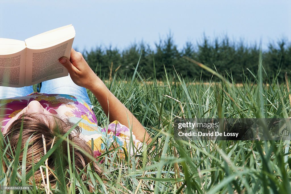 Young woman lying on field, reading book, ground view