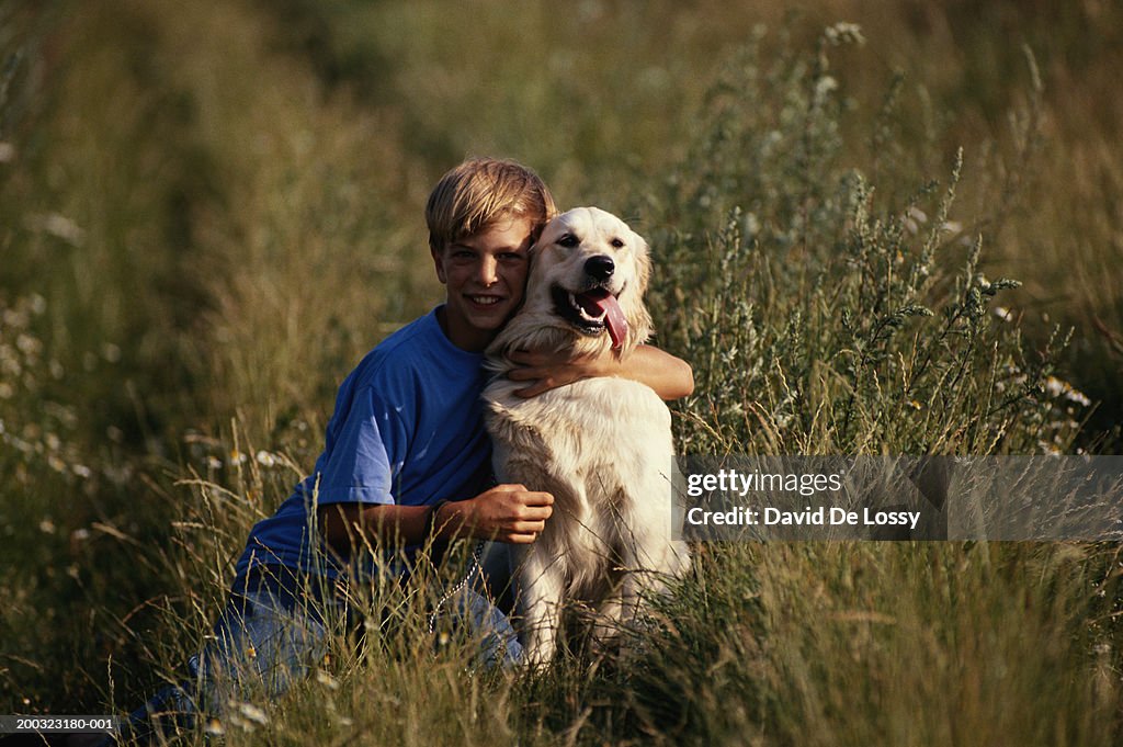 Boy (10-12) embracing dog in field