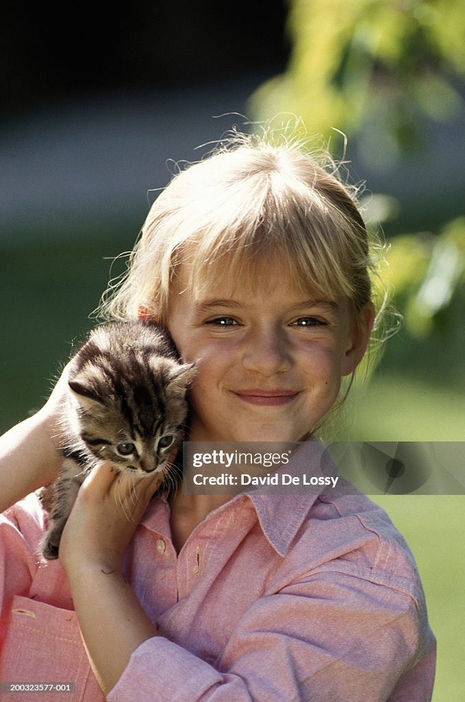 Girl (6-7) holding cat on shoulder, smiling