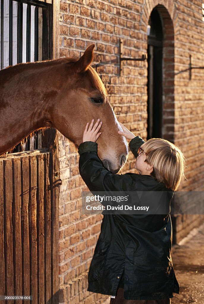 Boy (6-7) stroking horse in stable