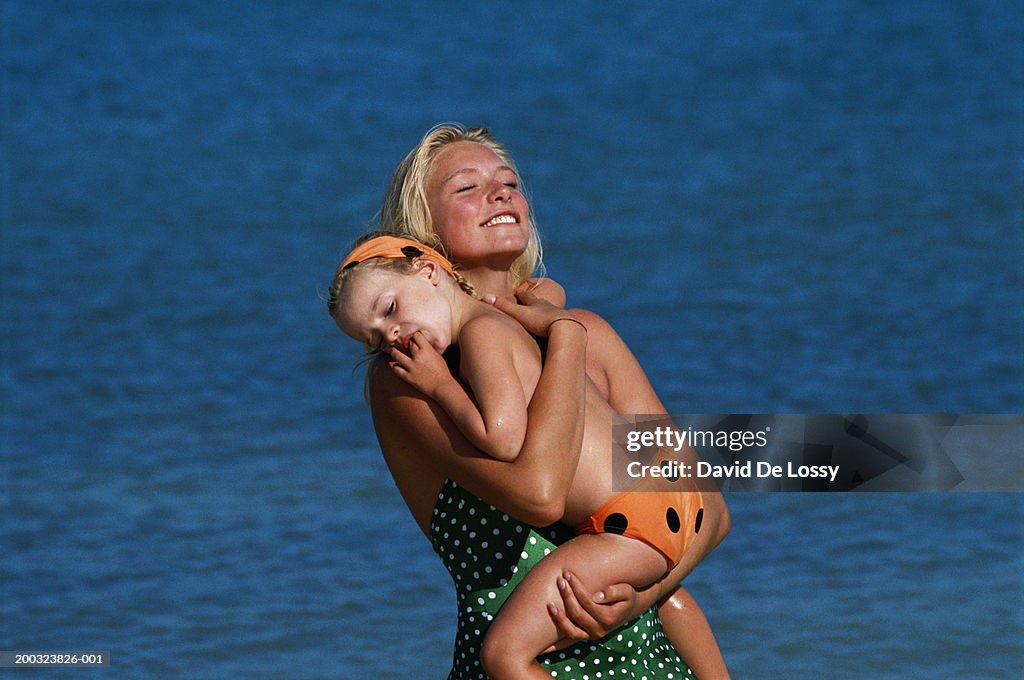 Mother carrying daughter (4-5) on beach, eyes closed