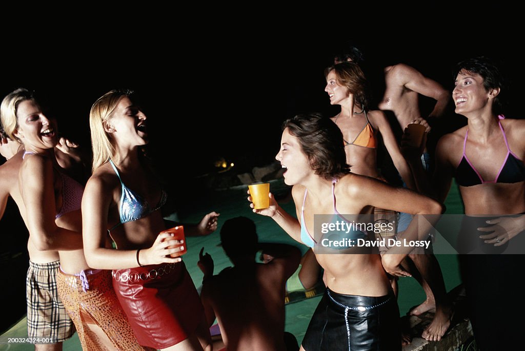 Group of people dancing poolside holding drinks