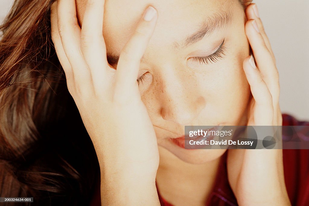 Young woman with eyes closed, head in hands, close-up