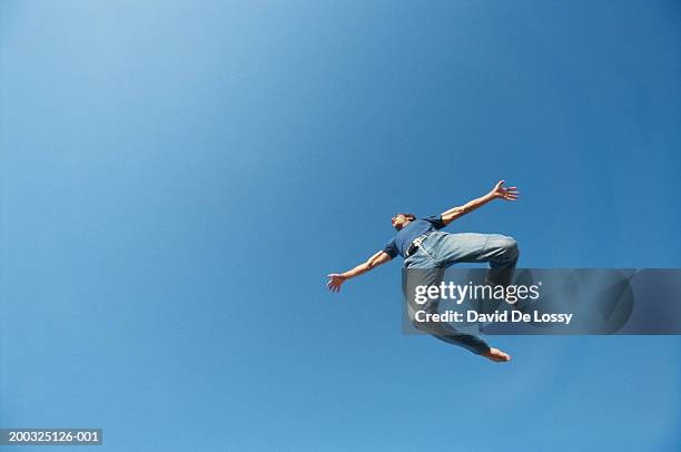 young man jumping, view from below - mann freudensprung sonne vorderansicht leger stock-fotos und bilder