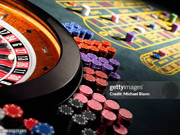 gambling chips stacked around roulette wheel on gaming table - casino fotografías e imágenes de stock