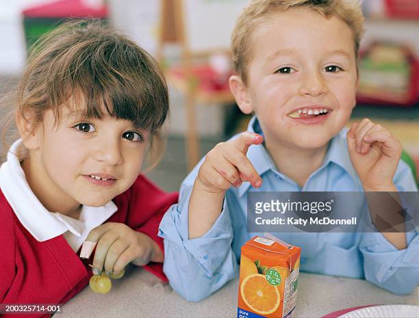 schoolgirl and boy (4-6) at table, smiling, close-up, portrait - ジュースパック ストックフォトと画像
