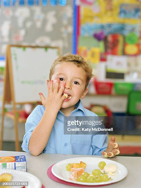 schoolboy (4-6) eating at table, wearing crisps on fingers, portrait - paper plate 個照片及圖片檔