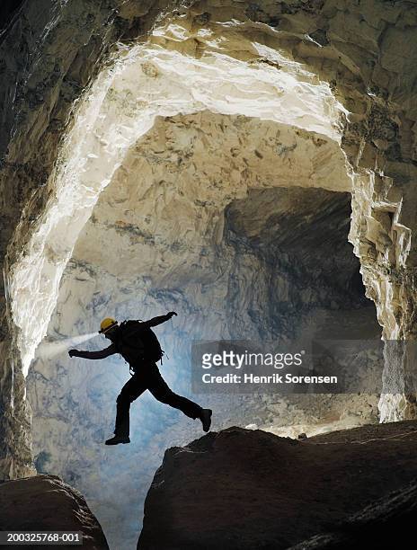 man jumping over crevasse in cave, side view - espeleología fotografías e imágenes de stock
