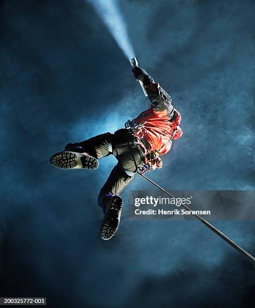 man abseiling in cave, holding torch, view from below - spelunking stock-fotos und bilder