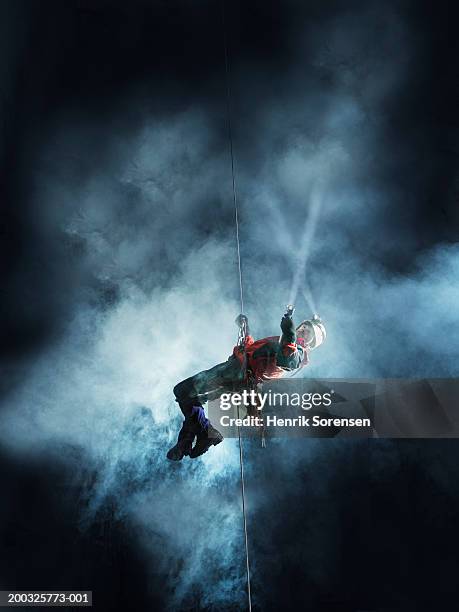 mature man abseiling in cave, holding torch - höhlenforscher stock-fotos und bilder