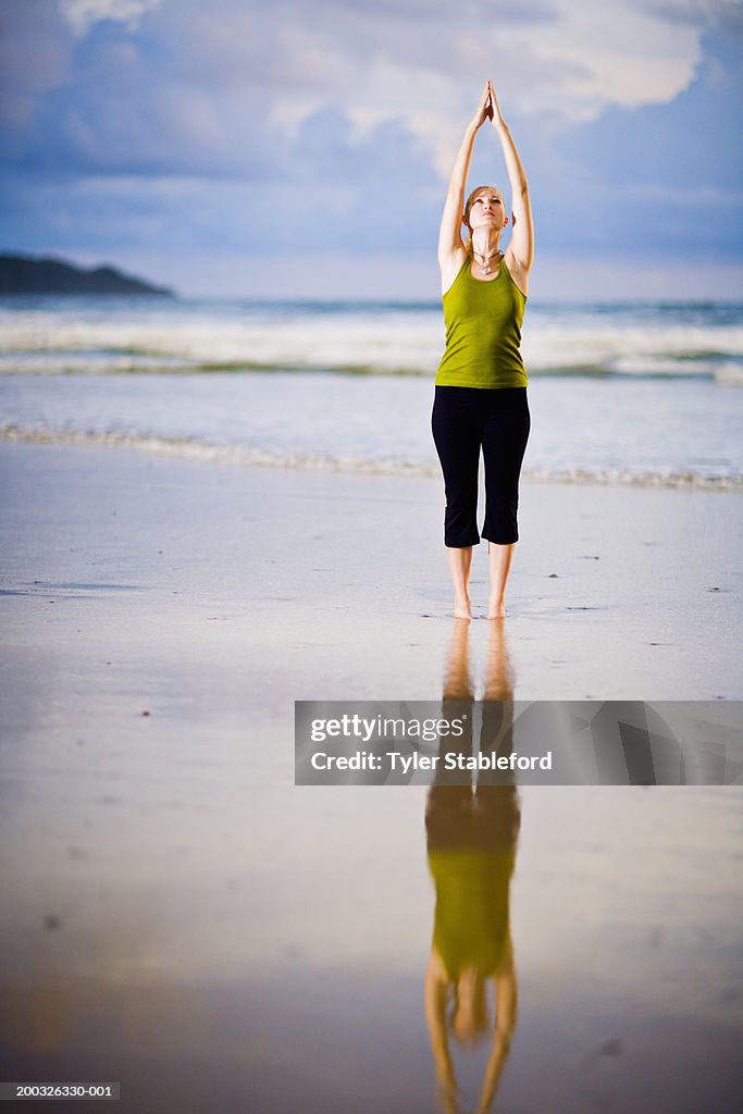 Young woman practicing yoga at beach, sunset