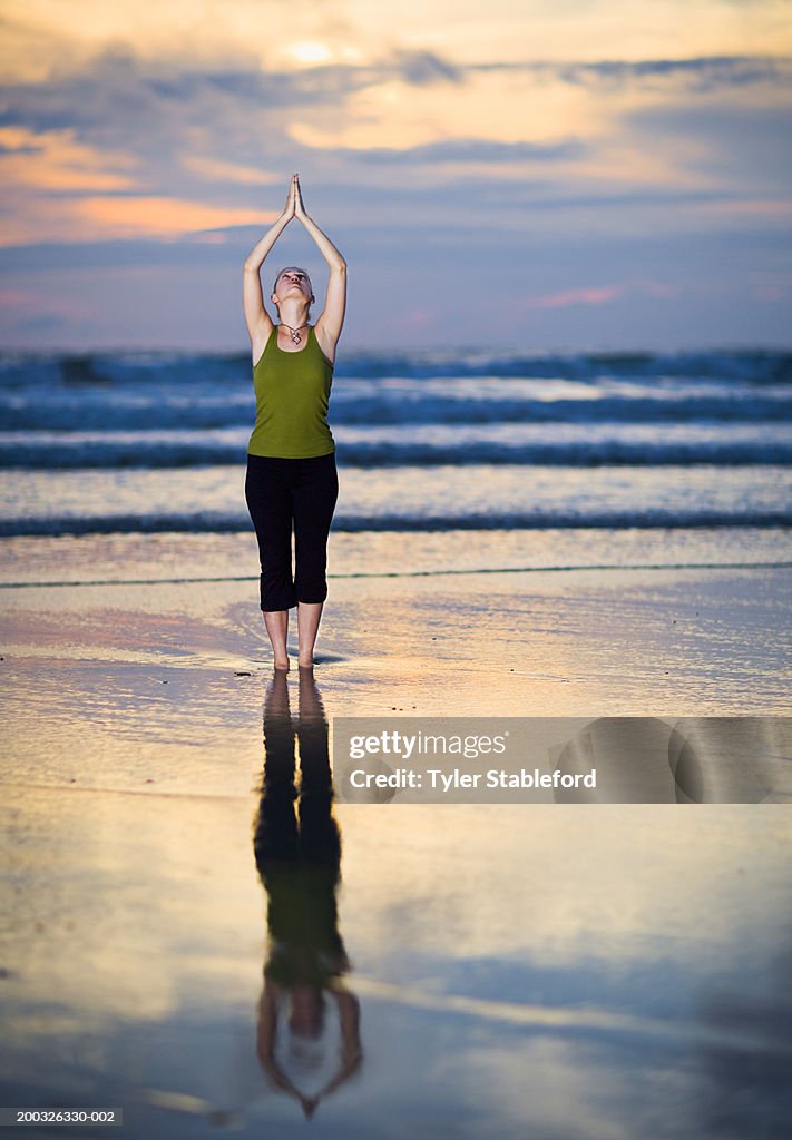 Young woman practicing yoga at beach, sunset, reflection in tidal zone