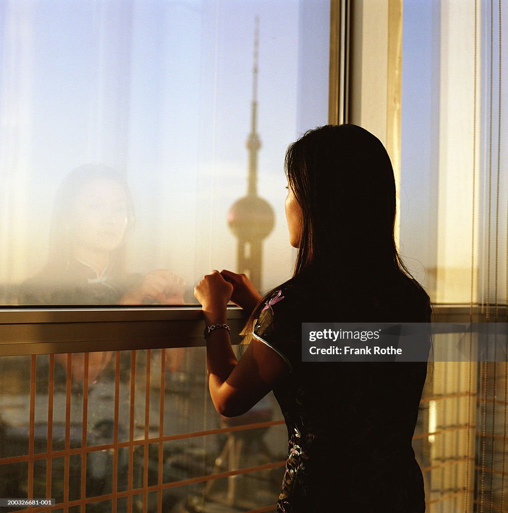 Young woman leaning on railing overlooking cityscape, dusk