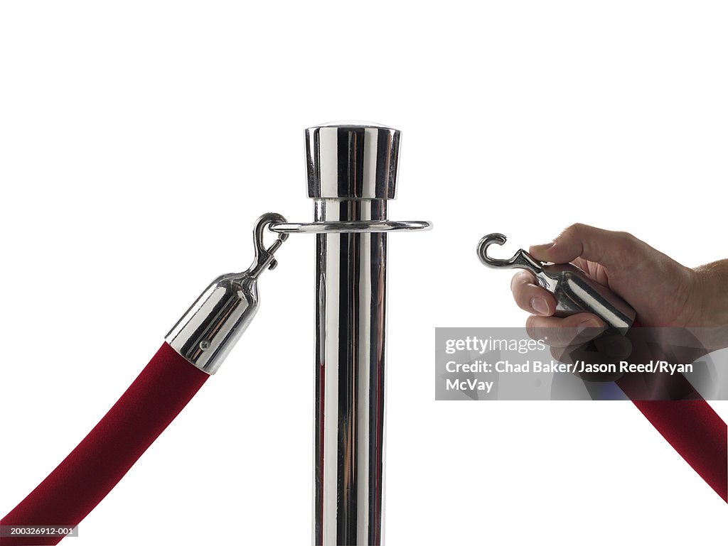 Man attaching velvet rope to barrier pole, close-up of hand