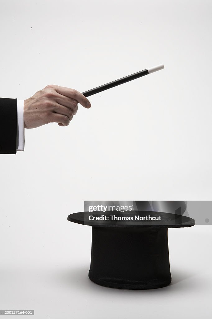 Man holding magic wand over top hat, close-up of hand, side view