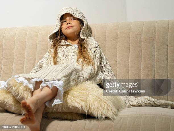 girl (6-8) wearing large hooded jumper, sitting on sofa - hood clothing stock pictures, royalty-free photos & images