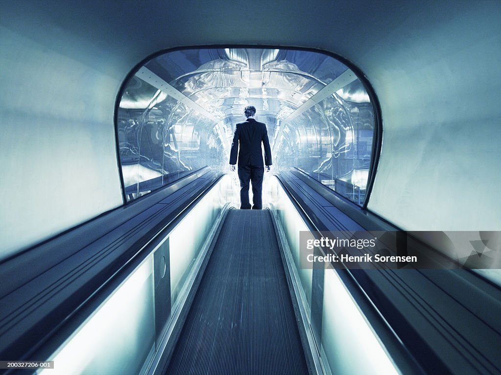 Man on escalator descending into tunnel, rear view