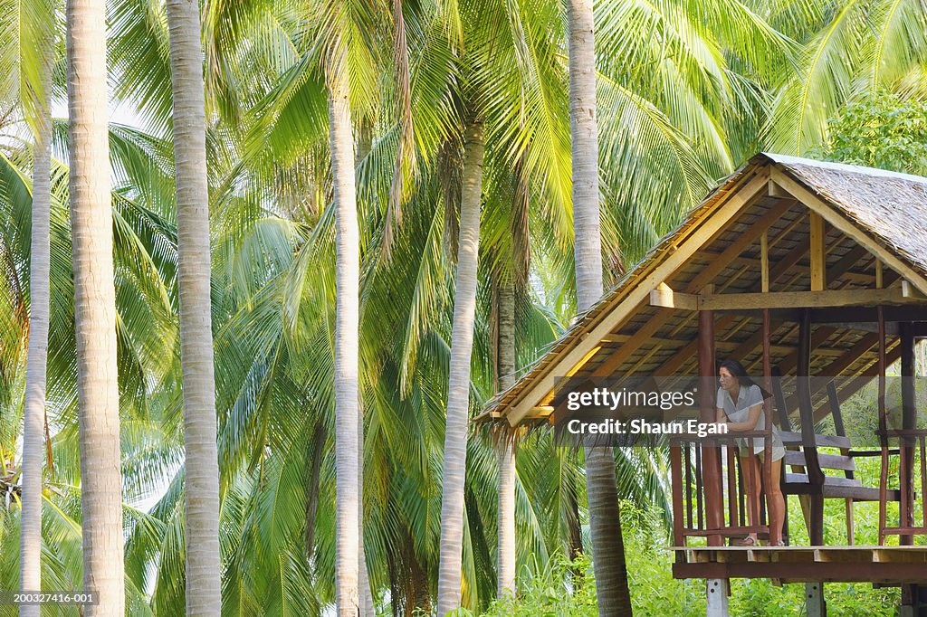 Woman leaning on railing of hut by palm trees
