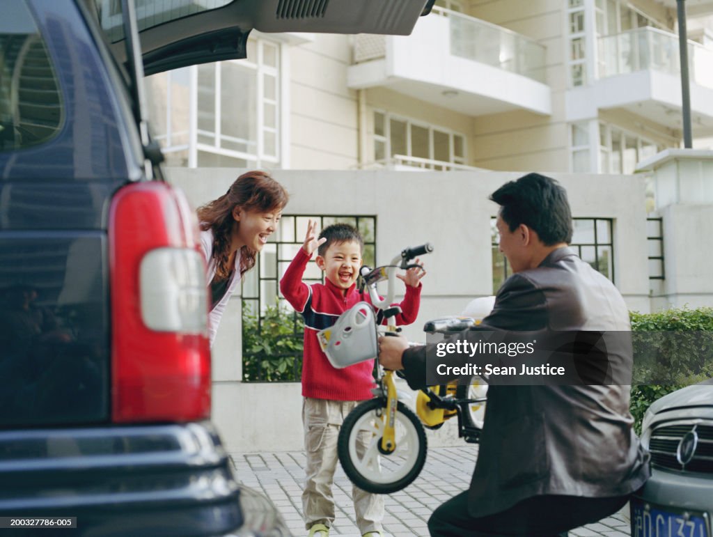 Father handing new bicycle to son (4-6), mother watching