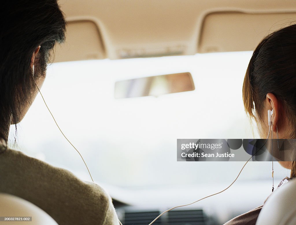Young man and teenage girl (17-19) sharing headphones, rear view