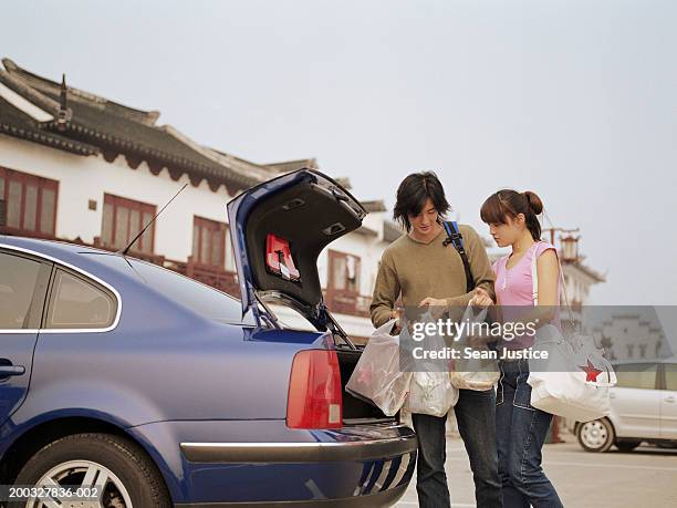 young couple removing shopping bags from car's trunk - shopping bags car boot stock pictures, royalty-free photos & images